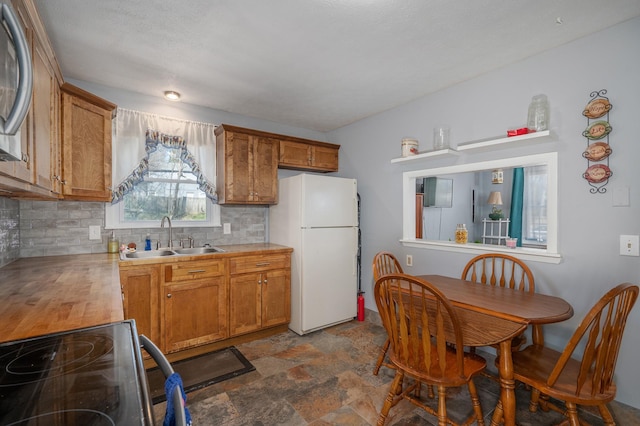 kitchen with stone finish flooring, decorative backsplash, brown cabinets, freestanding refrigerator, and a sink