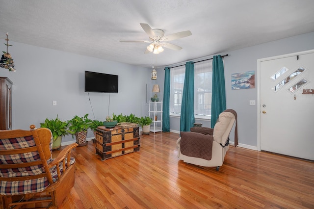 living area featuring baseboards, ceiling fan, and light wood finished floors