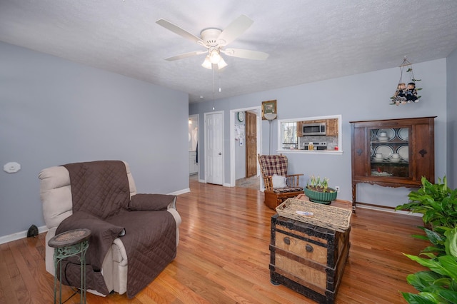 living area with baseboards, a textured ceiling, and wood finished floors