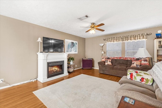 living area featuring visible vents, wood finished floors, a textured ceiling, and a glass covered fireplace