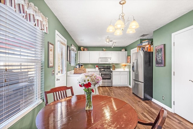 dining space with visible vents, a notable chandelier, a textured ceiling, wood finished floors, and baseboards