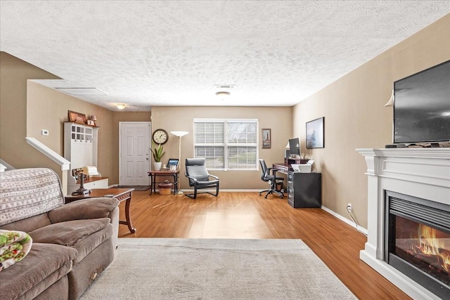 living area featuring visible vents, a textured ceiling, wood finished floors, a glass covered fireplace, and baseboards