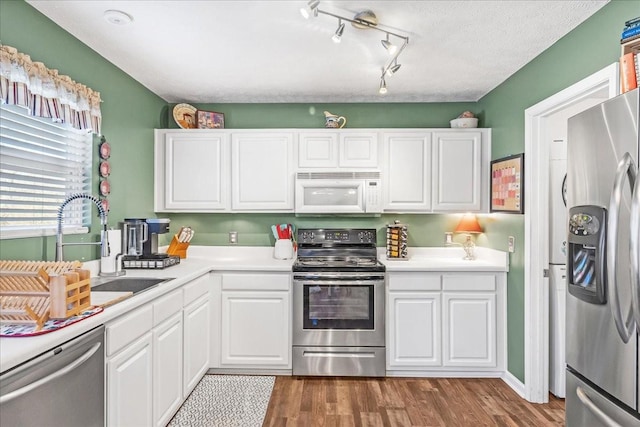 kitchen with a sink, dark wood-style floors, stainless steel appliances, white cabinets, and light countertops