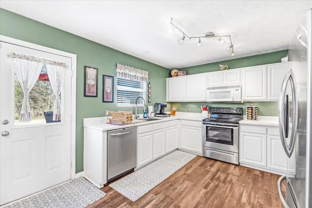 kitchen with wood finished floors, a sink, stainless steel appliances, light countertops, and white cabinets