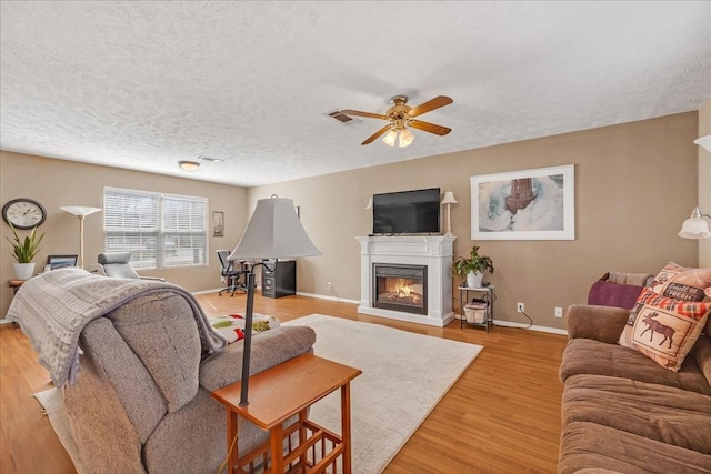 living room featuring visible vents, a textured ceiling, a glass covered fireplace, light wood finished floors, and baseboards