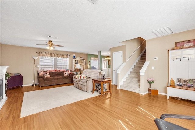 living room with a glass covered fireplace, stairway, visible vents, and wood finished floors