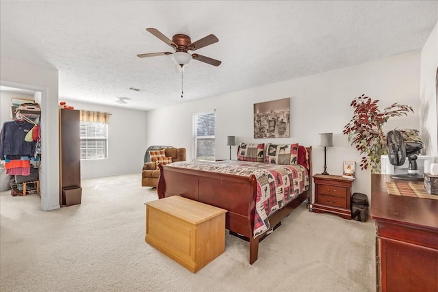 bedroom featuring a textured ceiling, visible vents, ceiling fan, light carpet, and a walk in closet