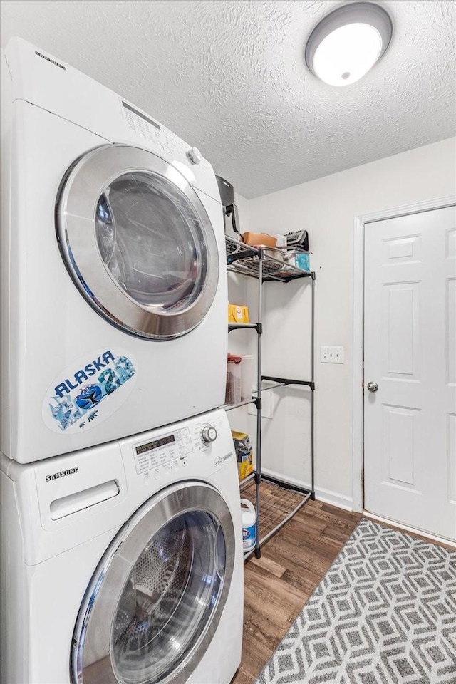 laundry area with baseboards, laundry area, stacked washing maching and dryer, wood finished floors, and a textured ceiling