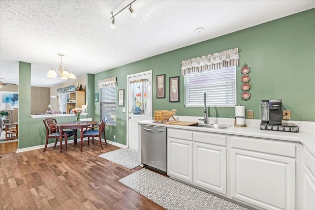 kitchen with stainless steel dishwasher, wood finished floors, white cabinets, a textured ceiling, and a sink