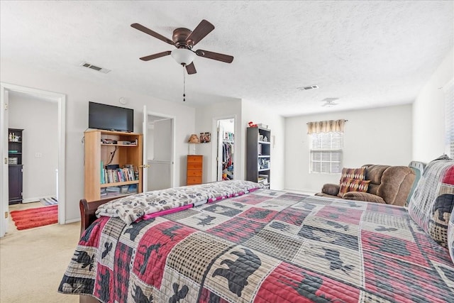 bedroom featuring a textured ceiling, a ceiling fan, visible vents, and light carpet