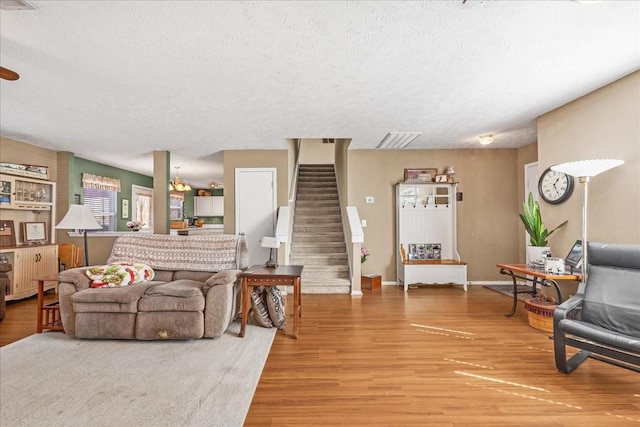 living area with stairway, light wood-style flooring, a textured ceiling, and visible vents