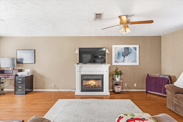 living area with a glass covered fireplace, visible vents, baseboards, and wood finished floors