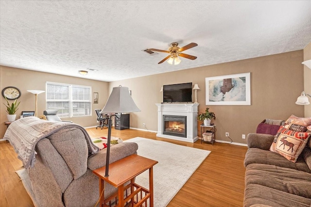 living room featuring a ceiling fan, baseboards, visible vents, a glass covered fireplace, and light wood-type flooring