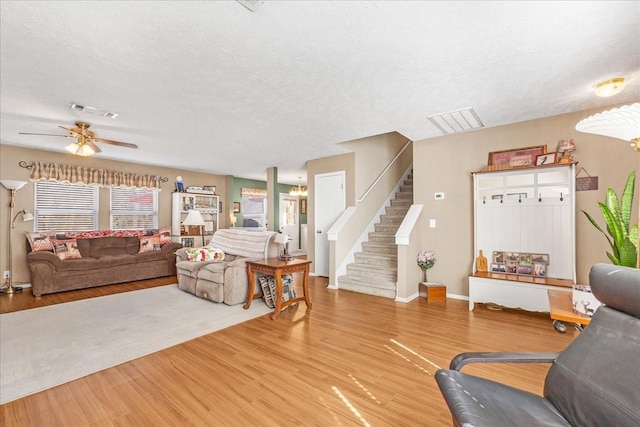 living area with stairs, visible vents, light wood finished floors, and a textured ceiling