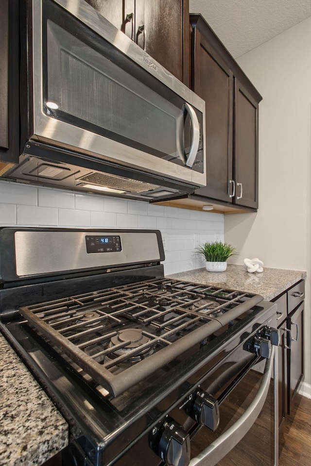 room details with dark brown cabinets, light stone counters, decorative backsplash, dark wood-style floors, and stainless steel appliances