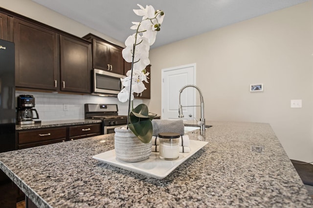 kitchen featuring dark brown cabinets, backsplash, stainless steel appliances, and dark stone counters