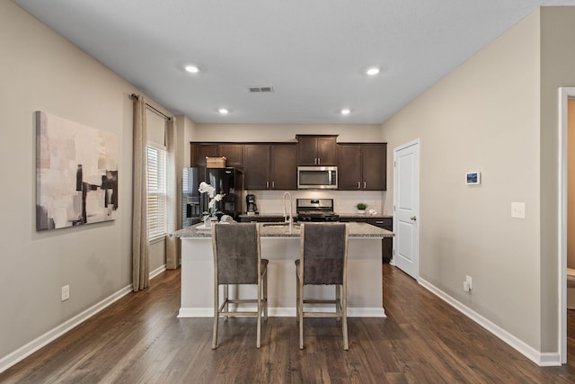 kitchen with visible vents, an island with sink, stainless steel appliances, dark brown cabinetry, and a breakfast bar area