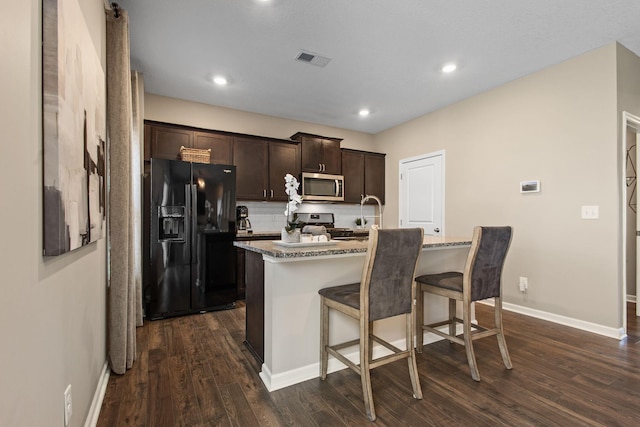 kitchen featuring visible vents, a kitchen breakfast bar, dark wood-style floors, dark brown cabinetry, and appliances with stainless steel finishes