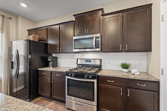 kitchen featuring light stone countertops, wood finished floors, stainless steel appliances, dark brown cabinets, and backsplash