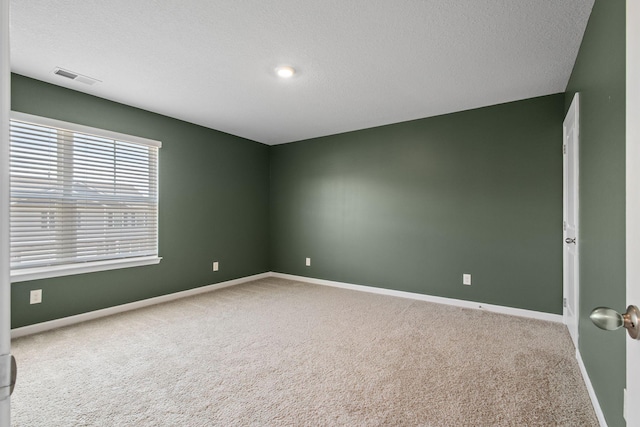 carpeted empty room featuring baseboards, visible vents, and a textured ceiling