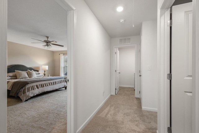 hallway featuring attic access, light colored carpet, visible vents, and baseboards