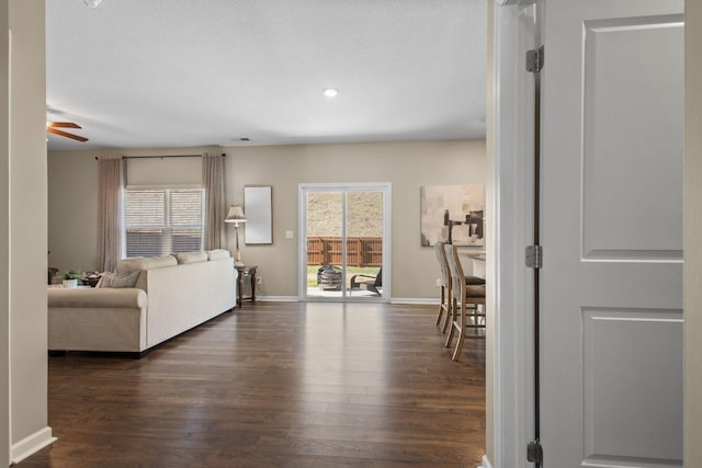 living room with dark wood-type flooring, plenty of natural light, baseboards, and ceiling fan