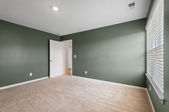 empty room featuring visible vents, carpet flooring, a textured ceiling, and baseboards