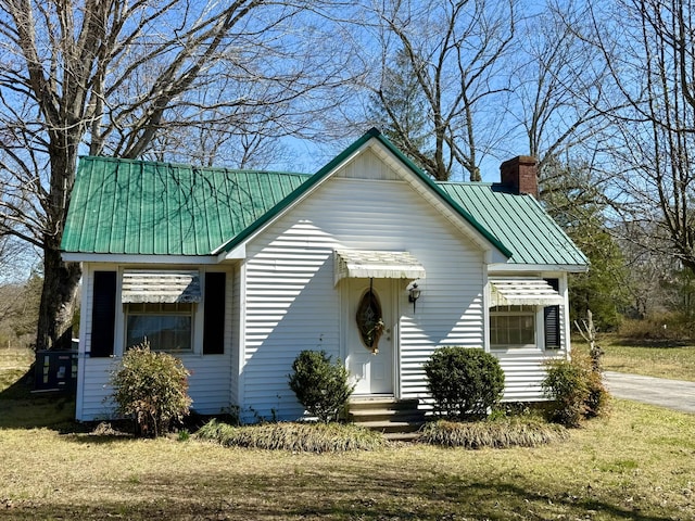 view of front facade featuring metal roof, a front lawn, a chimney, and entry steps