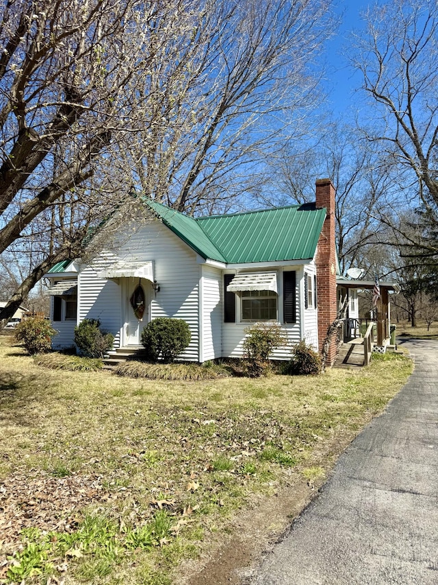 view of front of home featuring a chimney, metal roof, and a front yard