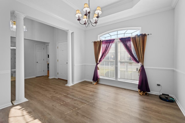 spare room featuring crown molding, wood finished floors, a raised ceiling, and decorative columns