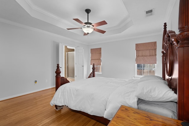 bedroom featuring light wood finished floors, visible vents, crown molding, baseboards, and a tray ceiling