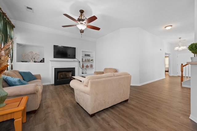 living room with built in shelves, wood finished floors, visible vents, a fireplace with flush hearth, and ceiling fan with notable chandelier