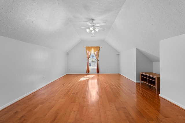 additional living space featuring lofted ceiling, light wood-style flooring, a ceiling fan, a textured ceiling, and baseboards