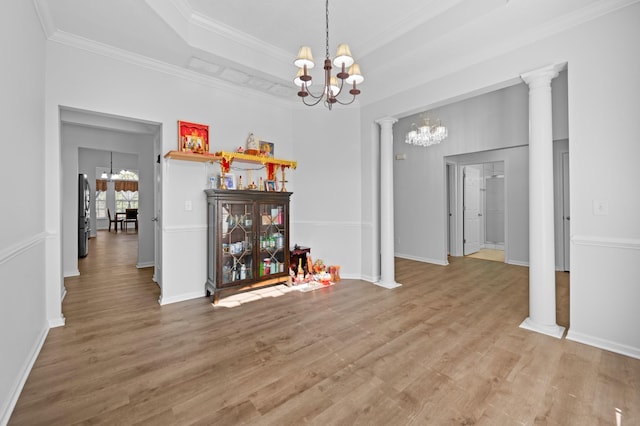 dining room featuring a tray ceiling, wood finished floors, a chandelier, and ornate columns