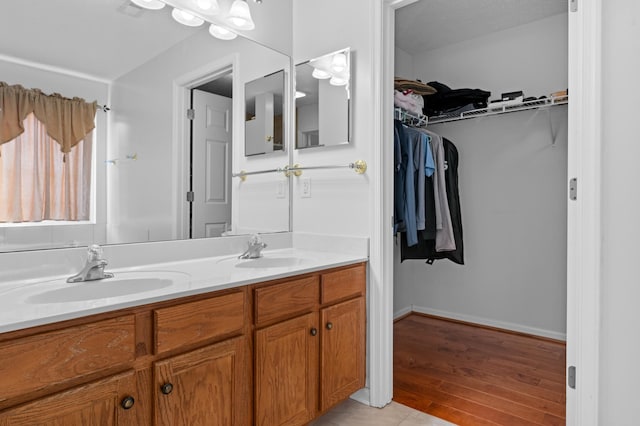 bathroom with a walk in closet, double vanity, wood finished floors, and a sink