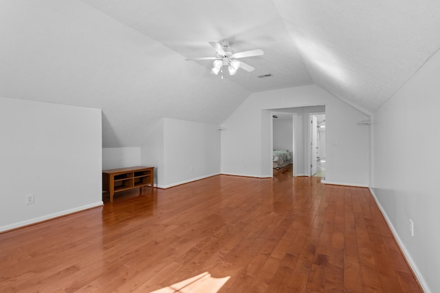 additional living space featuring visible vents, baseboards, lofted ceiling, light wood-style flooring, and a ceiling fan