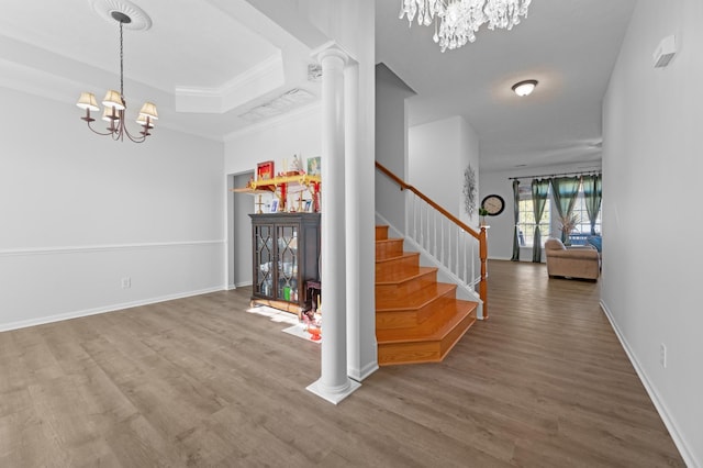 foyer with wood finished floors, decorative columns, a raised ceiling, a chandelier, and stairs