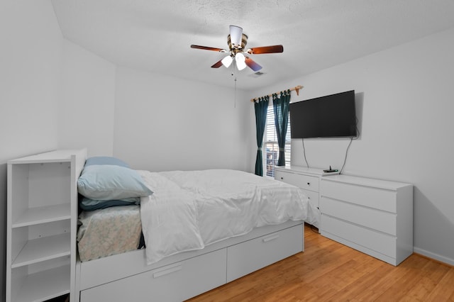 bedroom featuring light wood-type flooring, visible vents, a textured ceiling, and a ceiling fan