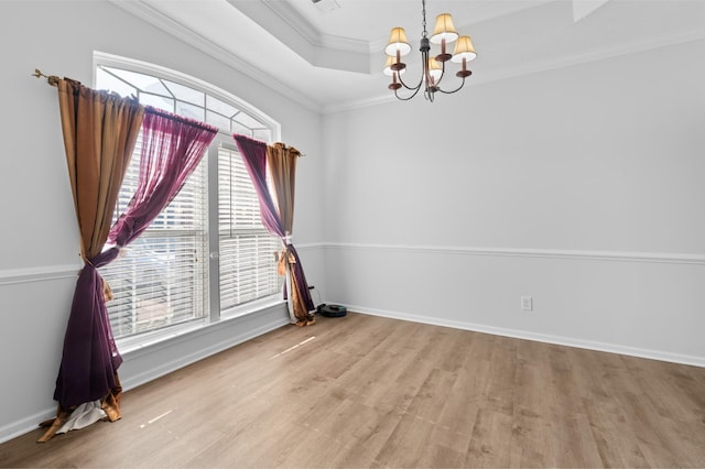 unfurnished room with wood finished floors, baseboards, a tray ceiling, crown molding, and a chandelier