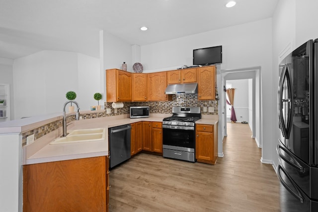 kitchen featuring under cabinet range hood, a sink, stainless steel appliances, light countertops, and decorative backsplash