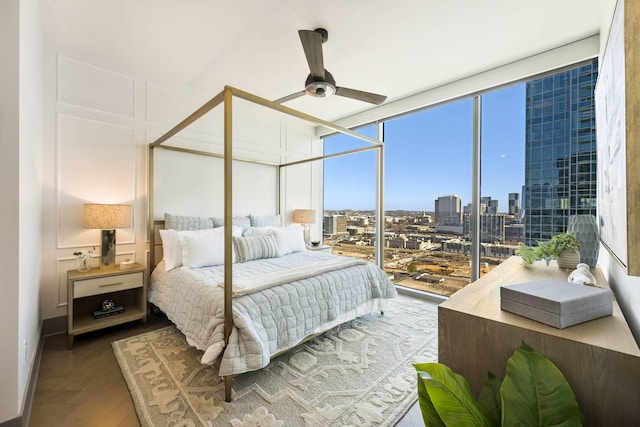 bedroom with wood finished floors, ceiling fan, floor to ceiling windows, a city view, and a decorative wall