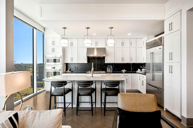 kitchen with a center island with sink, white cabinets, a kitchen breakfast bar, tasteful backsplash, and stainless steel built in refrigerator