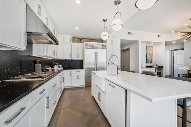 kitchen with a sink, appliances with stainless steel finishes, under cabinet range hood, white cabinetry, and tasteful backsplash