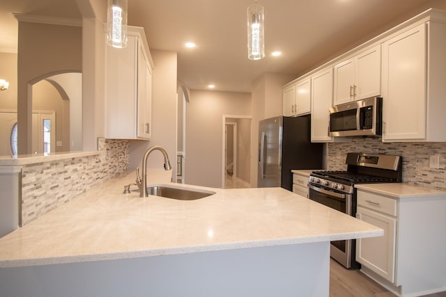 kitchen with a peninsula, a sink, stainless steel appliances, white cabinets, and backsplash