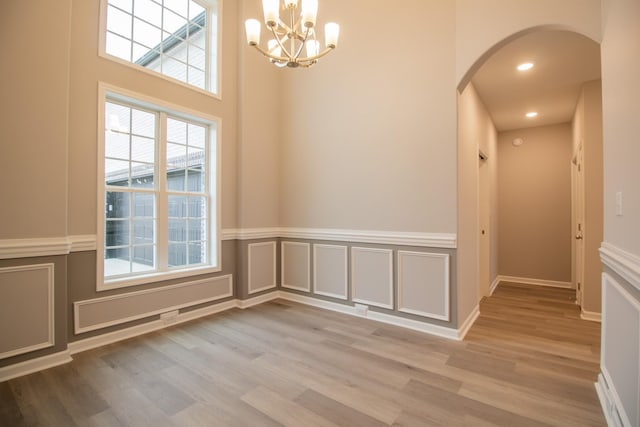 unfurnished dining area featuring a wainscoted wall, arched walkways, wood finished floors, and a decorative wall