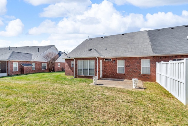 back of property with a shingled roof, a patio area, a lawn, fence, and brick siding