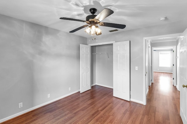 unfurnished bedroom with a closet, baseboards, visible vents, ceiling fan, and wood finished floors