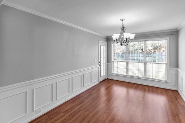 unfurnished dining area with a wainscoted wall, dark wood-style flooring, an inviting chandelier, and crown molding