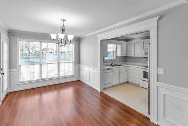 kitchen featuring an inviting chandelier, white appliances, ornamental molding, light countertops, and a sink