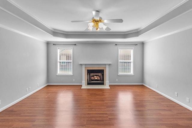unfurnished living room featuring a tiled fireplace, ceiling fan, wood finished floors, and a raised ceiling
